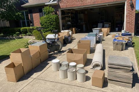 Boxes, paint cans, and carpet staged on a driveway during a garage cleanout